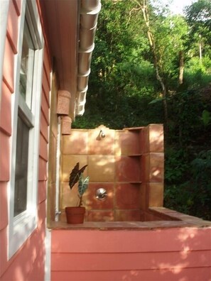 A small outdoor hot tub attached to a house with a window and a potted plant.