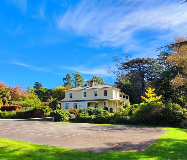 A two-story house with a tennis court in front.