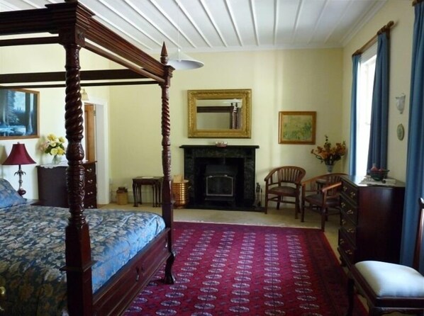 A bedroom with a four-poster bed, a fireplace, a mirror, and a red patterned carpet.