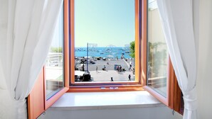Vista sulla baia da una finestra con tende bianche, cielo sereno e barche sull'acqua.