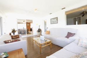 A living room with a white sofa, a glass-top coffee table, and a guitar.