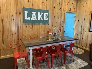 A wooden-paneled room with a table and red chairs, a sign reading "LAKE", and a door in the background.