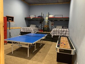 A room with bunk beds, a ping pong table, and a foosball table.