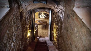 Un escalier étroit en pierre mène à une pièce ornée d’un lustre et d’un meuble à bouteilles.
