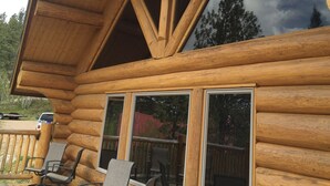 Una cabaña de troncos con terraza de madera, ventanas grandes y mobiliario exterior.