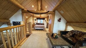Un dormitorio acogedor en el ático con techo de madera, una cama, una mesita de noche y vista al área de estar.