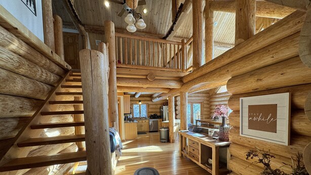 Interior de una cabaña de troncos con una escalera de madera, una zona de cocina y un comedor.