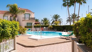 A pool area with lounge chairs, a white fence, and palm trees.