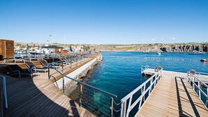 A wooden pier with lounge chairs and a view of the marina and rocky coastline.