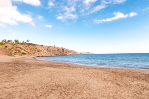 A sandy beach with a clear sky and a rocky cliff.