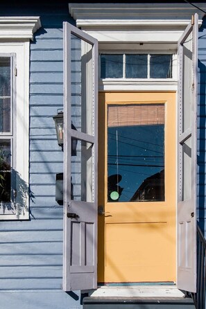 A house with a yellow door and white trim, a small porch, and a window with shutters.
