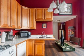 A compact kitchen with wooden cabinets, a microwave, a sink, and a wine bottle on the counter.