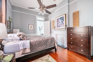 A bedroom with a bed, dresser, ceiling fan, and artwork on the walls.