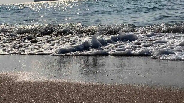 Una playa con olas rompiendo en la orilla y dos grandes formaciones rocosas al fondo.