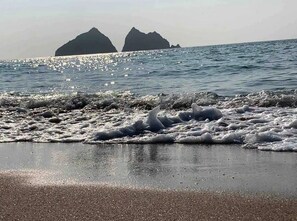 A beach with waves crashing onto the shore and two large rock formations in the background.
