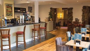 Un restaurante con una zona de bar, sillas y mesas de madera.