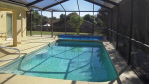 A covered swimming pool with a clear blue water surface, surrounded by a metal fence and a shaded area.