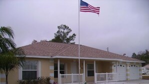 A single-story house with a front porch, a garage, and a flagpole with an American flag.