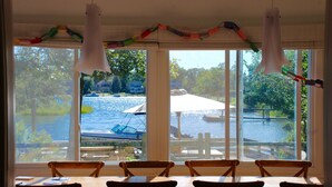 A dining area with a view of a lake and boats, featuring a table and chairs, and a hanging light fixture. - Hamptons Waterfront Beach Home With Dock (Southampton)