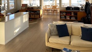 A spacious loft with a high ceiling, a dining area, a kitchen, and a cozy seating area with a sofa and cushions. - Hamptons Waterfront Beach Home With Dock (Southampton)