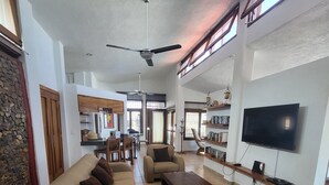 A spacious living room with a large sofa set, a coffee table, and a flat-screen TV mounted on the wall.