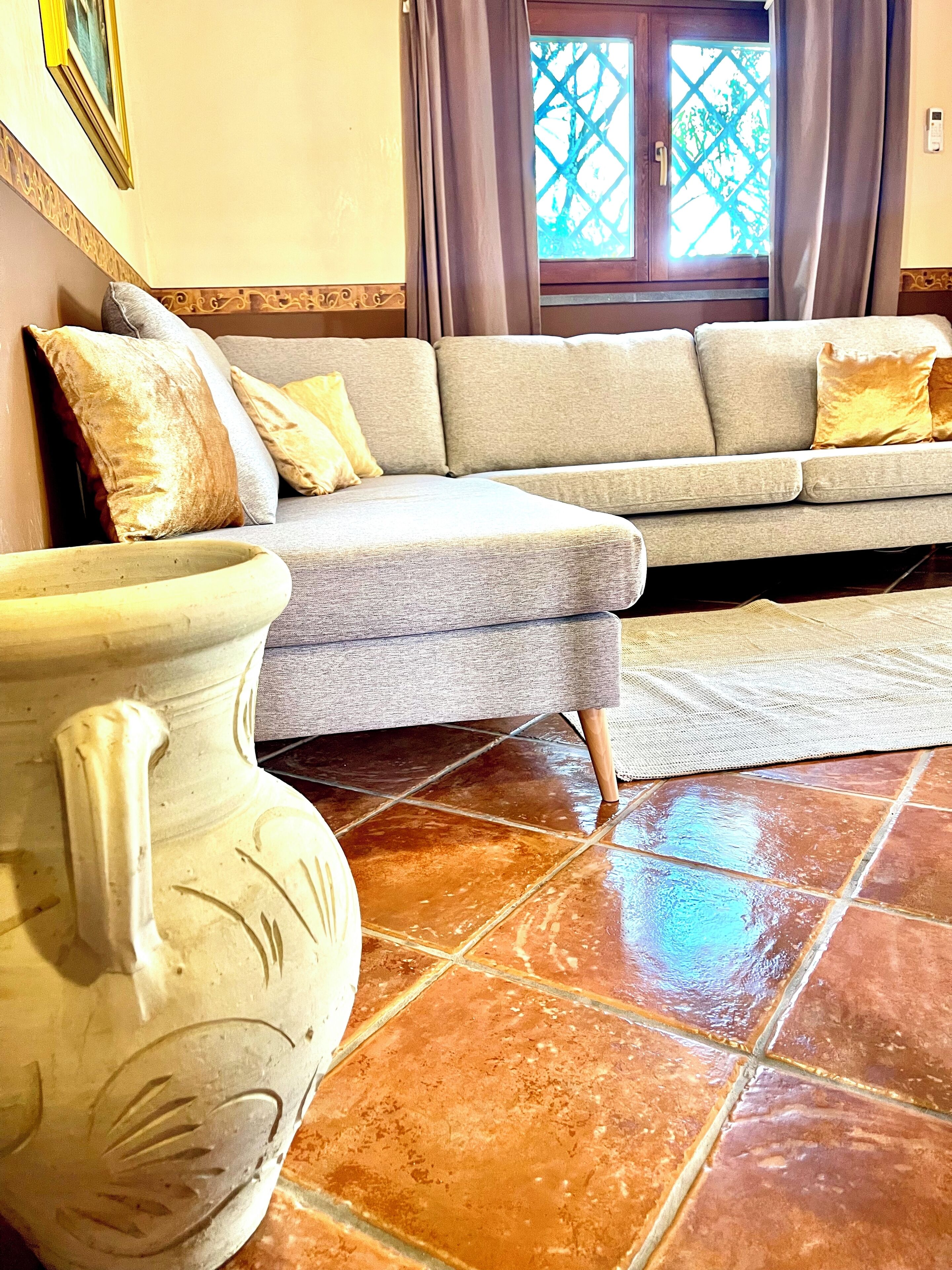 A living room with a grey sofa, a large white vase, and a tiled floor.