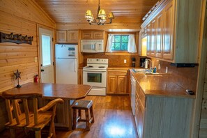 A wooden cabin interior with a kitchen featuring a stove, microwave, refrigerator, and wooden cabinets.
