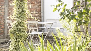 A brick wall with a white door, a white table and chairs, and green plants. - Apartment/studio (converted barn, 40 sqm) with gallery (Schernfeld)