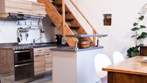 A modern kitchen with wooden cabinets, a built-in oven, a stainless steel range hood, and a wooden staircase. - Apartment/studio (converted barn, 40 sqm) with gallery (Schernfeld)