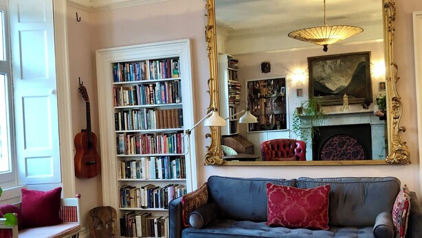 A cozy living room with a blue sofa, a large bookshelf, a guitar, and a patterned rug. - Central Georgian Home with Parking, Art and Antiques (Edinburgh)