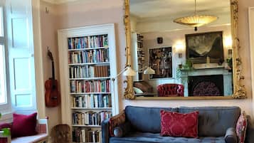 A cozy living room with a blue sofa, a large bookshelf, a guitar, and a patterned rug.