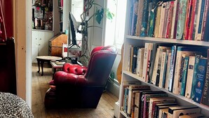 A cozy reading nook with a red armchair, a bookshelf filled with books, and a wooden floor. - Central Georgian Home with Parking, Art and Antiques (Edinburgh)