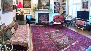 A living room with a fireplace, a sofa, a red armchair, a television, and a bookshelf. - Central Georgian Home with Parking, Art and Antiques (Edinburgh)