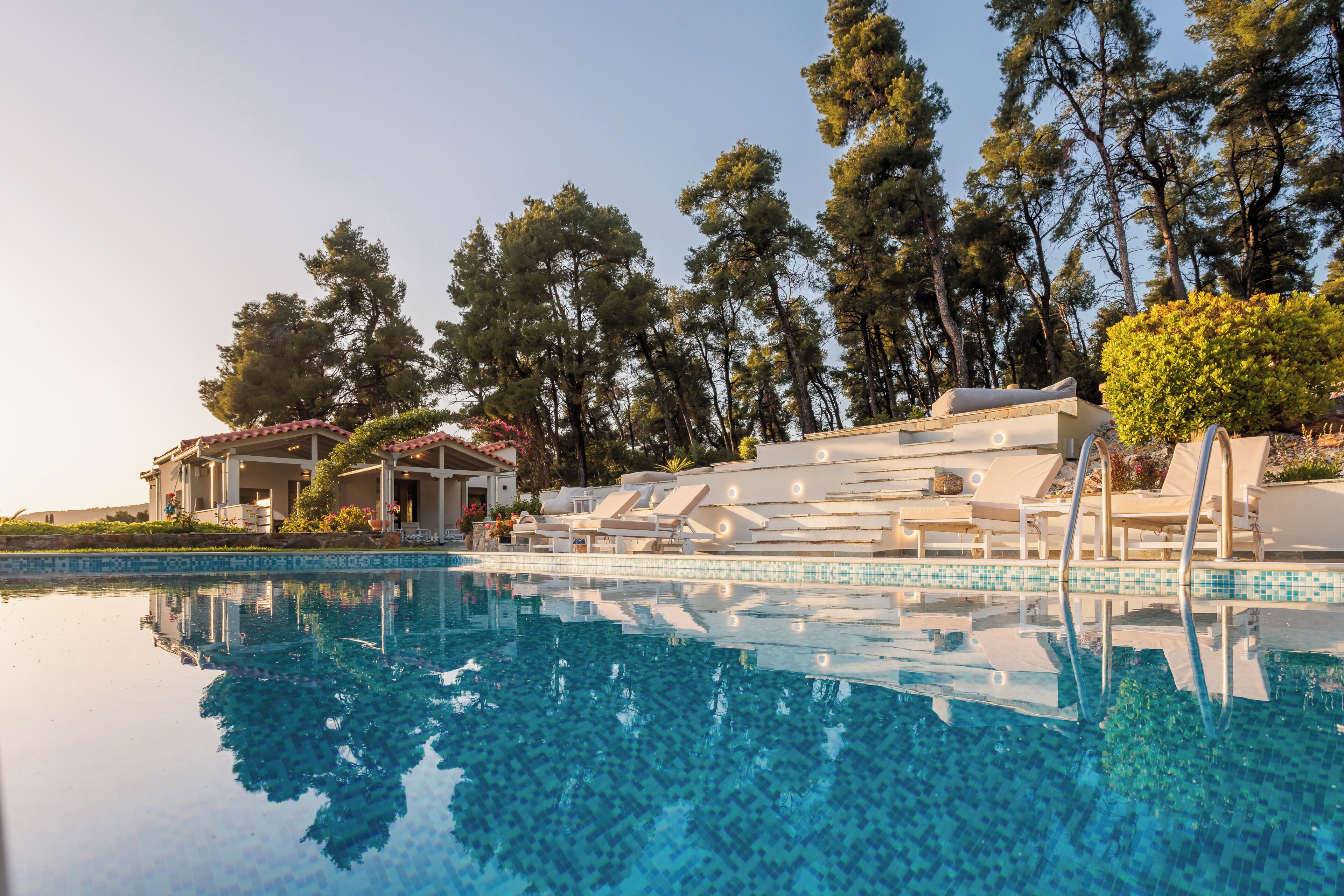 A swimming pool with lounge chairs, a covered seating area, and a building with a tiled roof.