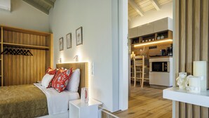 Ett modernt hotellrum med en säng, sängbord, en lampa, en träpanel vid sänggaveln, ett köksutrymme med vitvaror och ett trägolv.