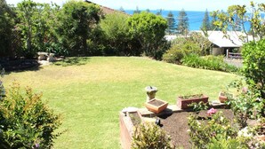 A well-maintained garden with a lawn, a birdbath, and a small brick planter with a plant. - High Street Retreat is set in the heart of Black Head & has magnificent... (Black Head)