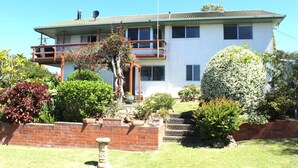 A two-story house with a balcony, surrounded by various shrubs and a small garden. - High Street Retreat is set in the heart of Black Head & has magnificent... (Black Head)