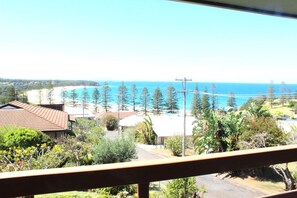 A coastal view from a balcony with a clear sky, a beach, and a row of pine trees. - High Street Retreat is set in the heart of Black Head & has magnificent... (Black Head)