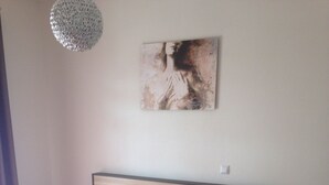 Un letto con biancheria bianca e rossa, una testata in legno, un comodino con una lampada e un'opera d'arte appesa al muro.