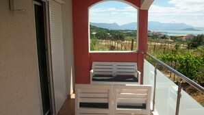 Un balcone con due sedie bianche, ringhiera in vetro e vista su un vigneto e montagne.