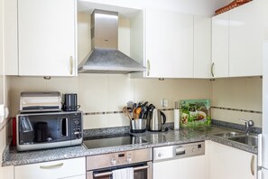 A kitchen with white cabinets, a stainless steel range hood, a microwave, a toaster, a coffee maker, and a set of kitchen utensils.