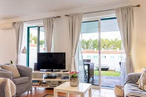 A living room with a flat-screen TV, a coffee table with a flower vase, and a sofa.