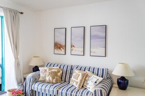 A room with a striped sofa, two lamps, and three framed pictures on the wall.