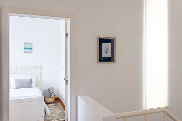 Une chambre à coucher avec un lit, une table de chevet, un tableau encadré au mur et une fenêtre avec des stores.