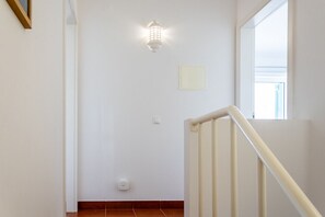 A staircase with a handrail, a light fixture on the wall, and a window with a view.