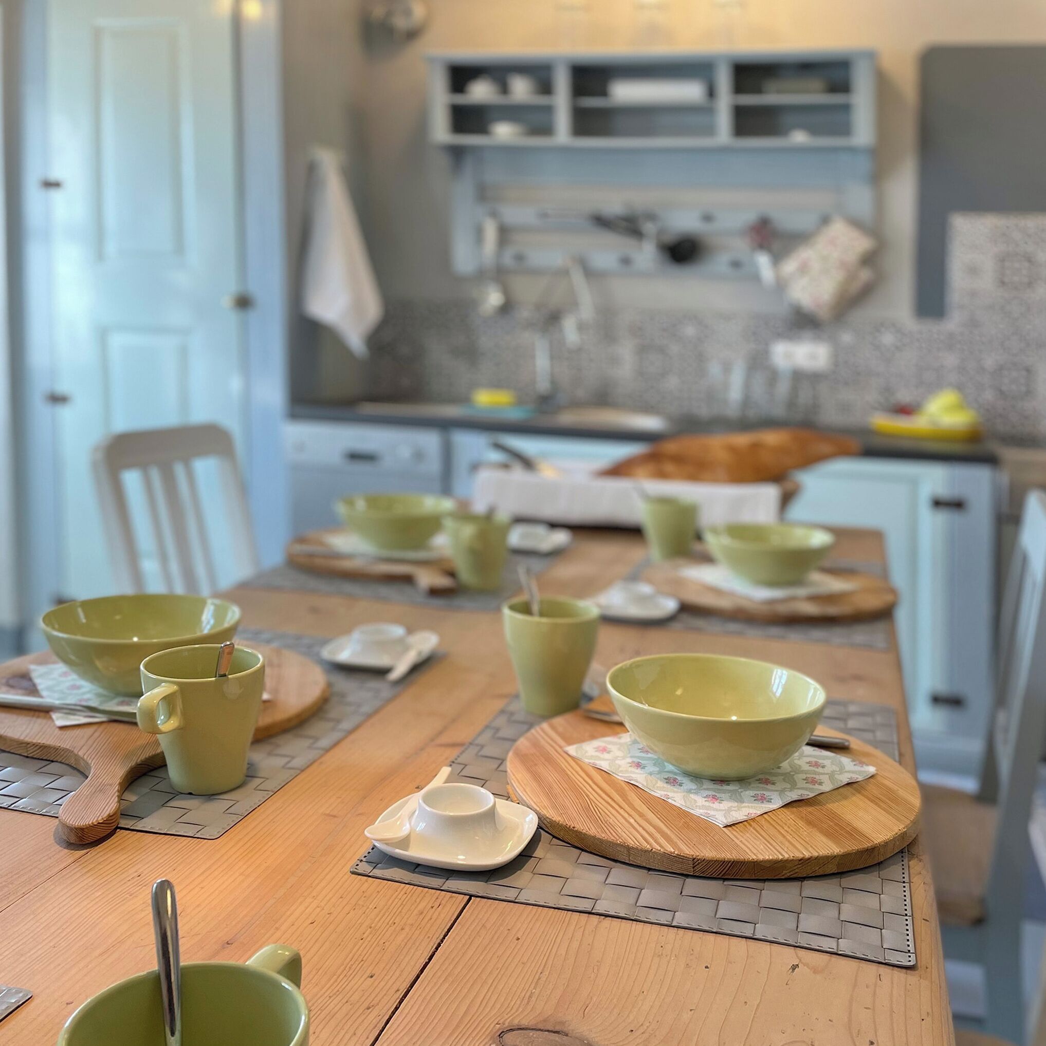 A dining table set with green bowls and spoons, wooden placemats, and a white plate.