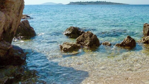 Un paysage côtier avec une eau claire, des formations rocheuses et une île au loin.