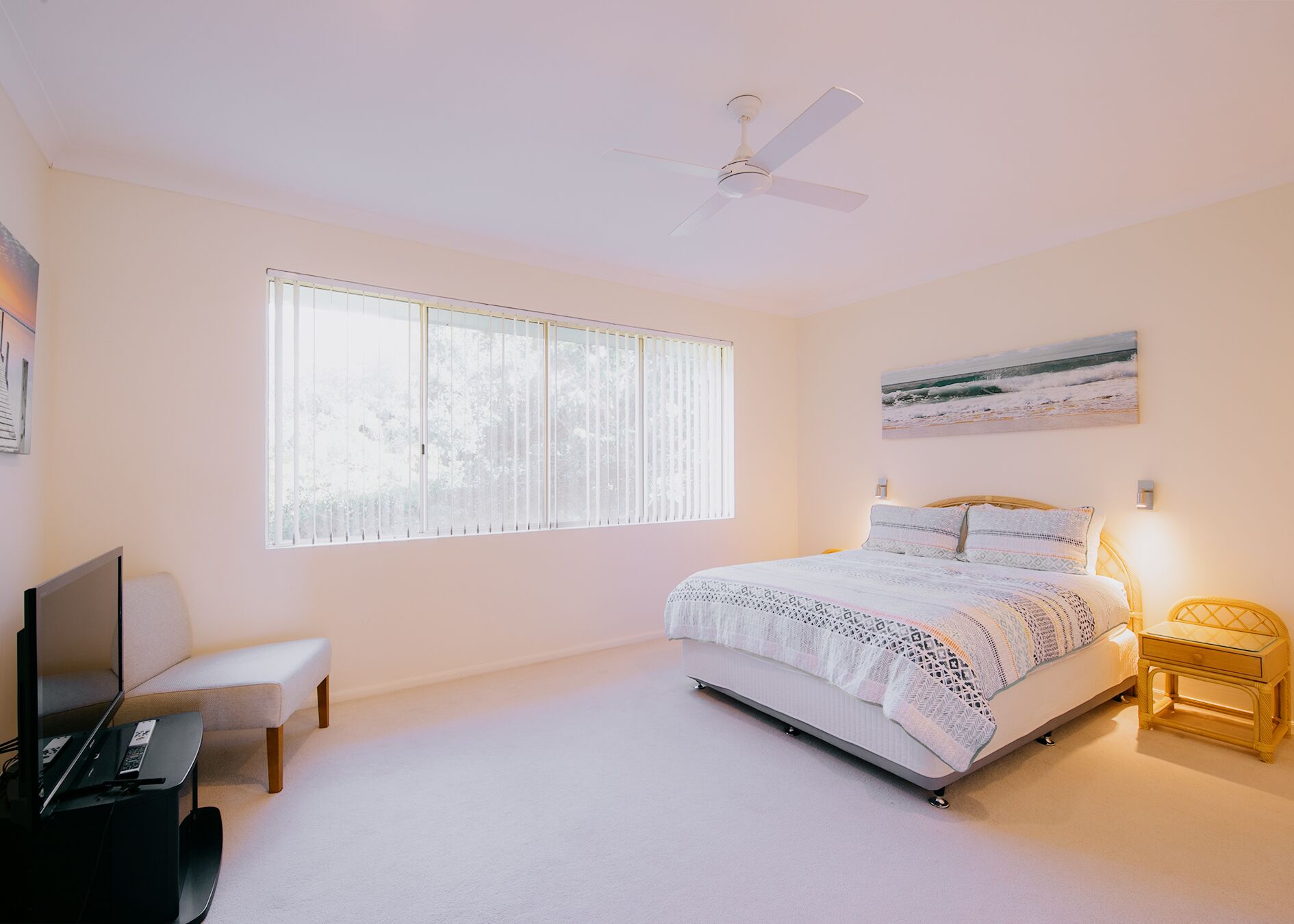 Une chambre à coucher comprenant un lit, un bureau, une chaise, un ventilateur de plafond et une fenêtre avec des stores.