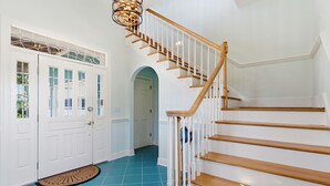 A staircase with wooden steps and white railings, leading to a landing with a white door and a blue-tiled floor.