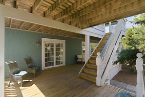A covered porch with a wooden staircase, wicker chairs, and a door leading to an interior space.